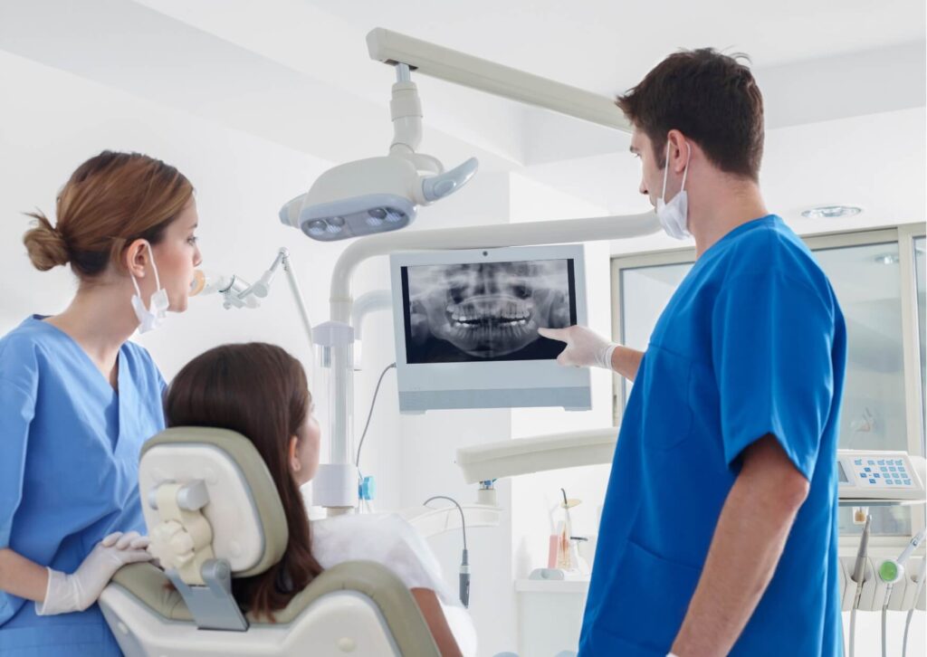 Dentist reviewing a panoramic X-ray with a patient to determine whether bone grafting is needed before a dental implant.