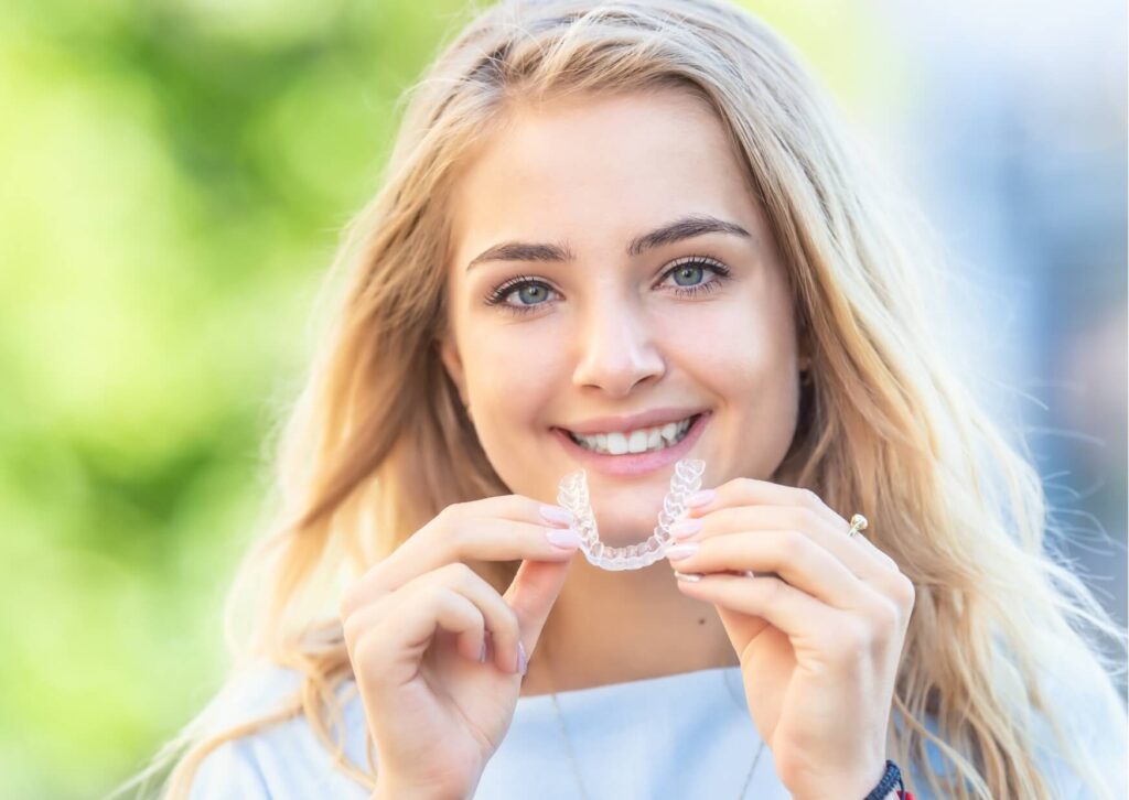 Teen smiling while holding clear aligners, illustrating Invisalign as a discreet alternative to braces for straightening teeth.